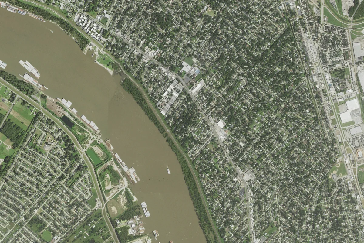 Aerial view of River Ridge's tree-lined streets along the Mississippi River, with the levee, barges at the bank and the west bank across the water